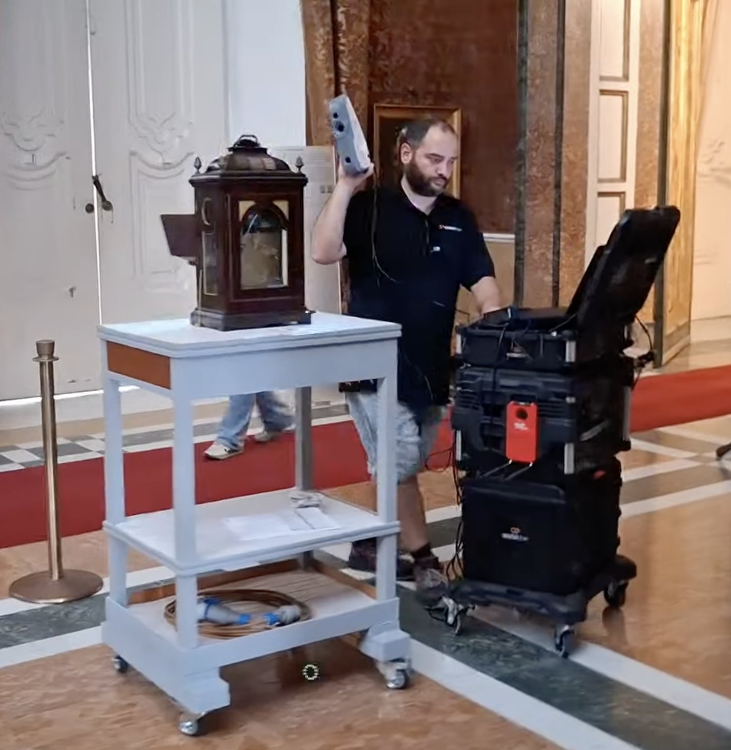 Ein mobiler Standort in einem Museumssaal: der Kit-Wagen neben einem vorbereiteten Tisch mit dem darauf liegenden Werk, der Operator scannt mit dem handgeführten Streifenlichtscanner